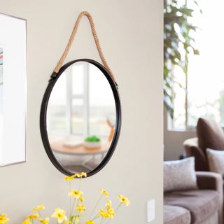 Round black framed mirror with rope handle on neutral wall