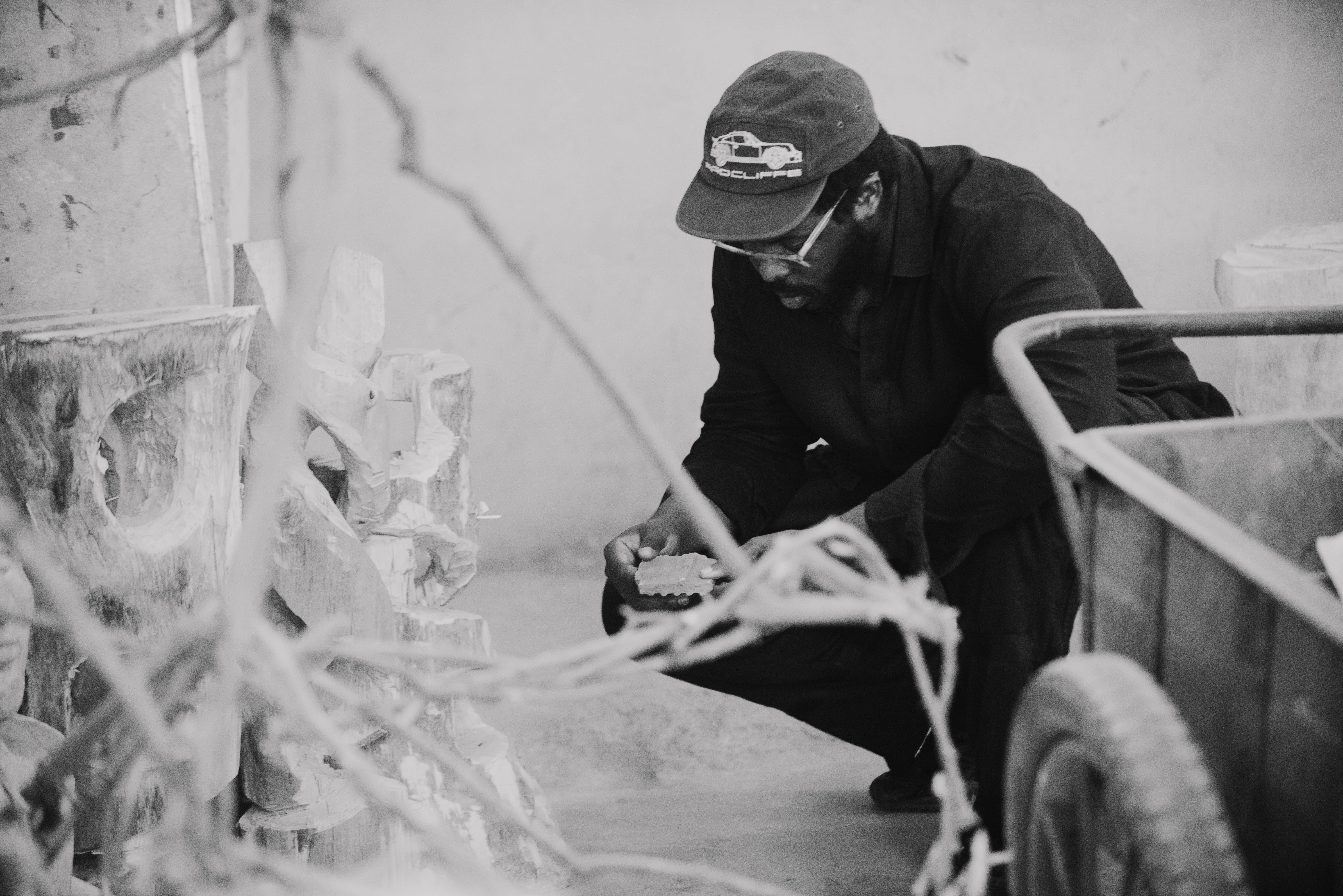 Designer Myles Igwebuike crouches o the floor next to artworks
