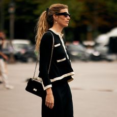 An attendee at Paris Fall Winter 2025, Haute Couture fashion week with a white and black sweater, sunglasses, and black crossbody bag