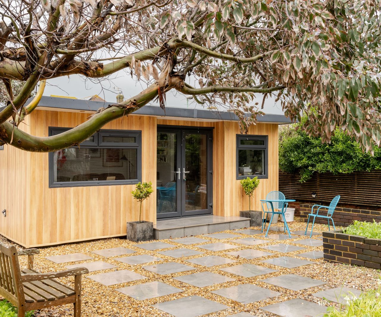 An outside garden shed with a gravelled path with a wooden clad garden room