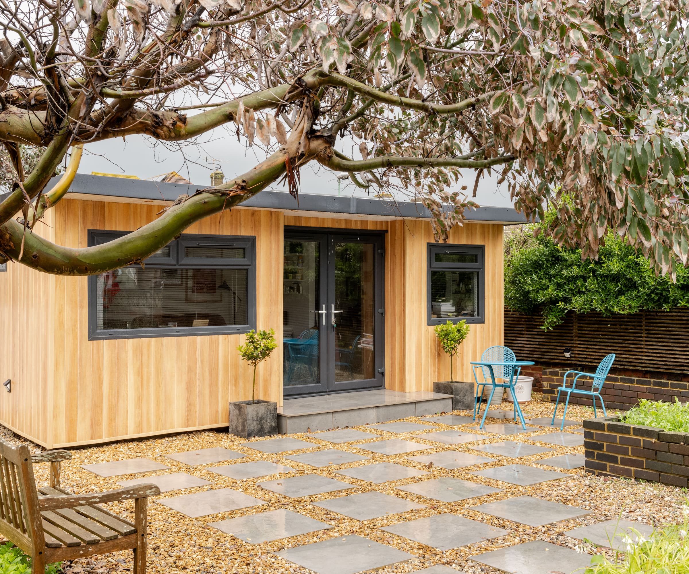 An outside garden shed with a gravelled path with a wooden clad garden room