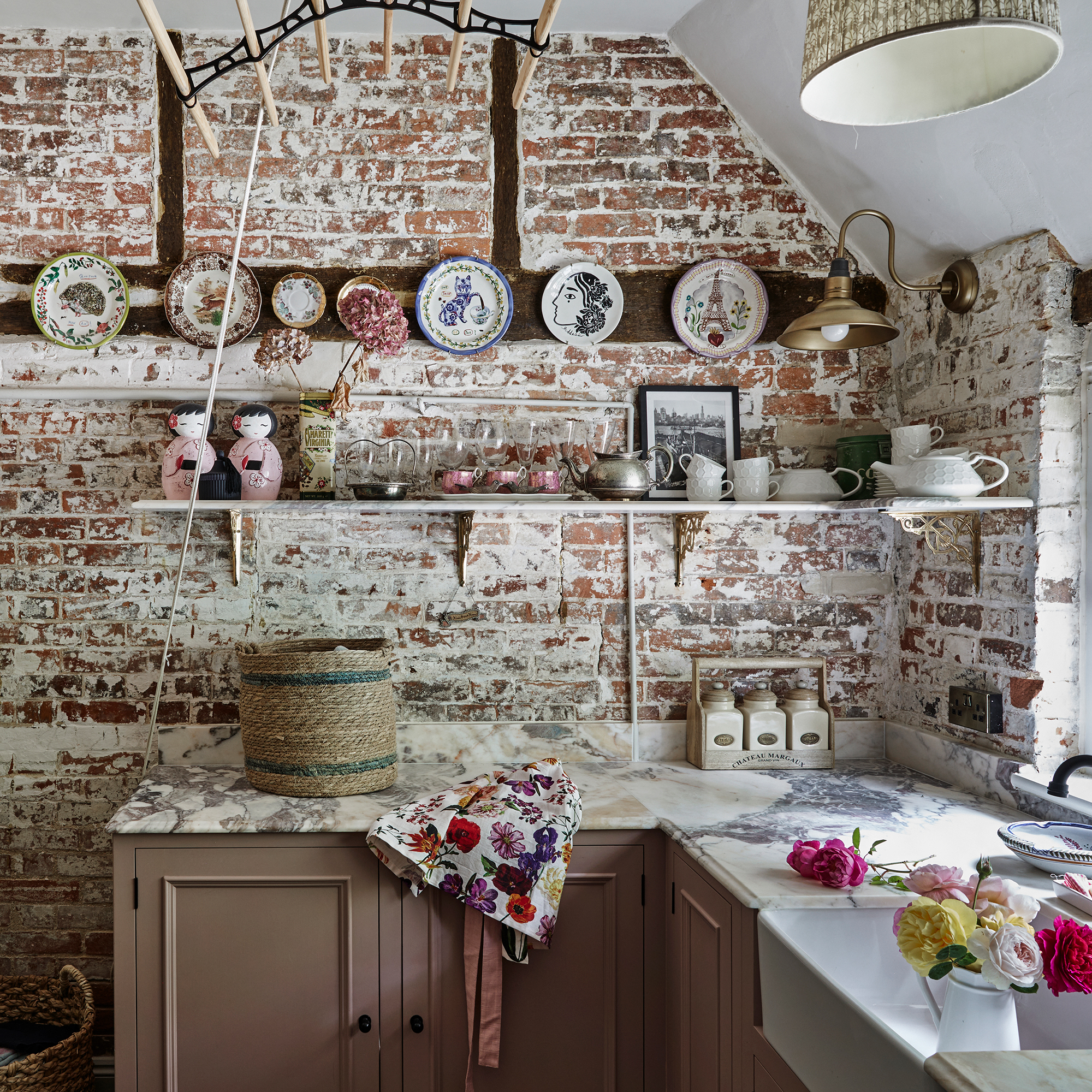 laundry room in a country house with limewashed brick walls, pink cupboards and marble worktops