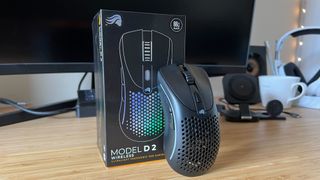 Glorious Model D 2 gaming mouse leaning on product box on a wooden desk setup