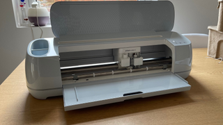 Best Cricut machines; a large white craft machine on a wooden table with its lid and draw open, it's blade cutter is visible