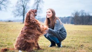 Woman crouched down on the grass smiling at her dog