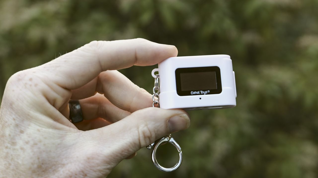 Miniature pink keychain camera, the 'Photo Creator Mini Digital Camera series 3', in user's hand, its rear screen