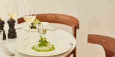 A restaurant table in marble and wood is complete with a white plate filled with a creamy broad beans and cheese starter, two white wine glasses, silver cutlery, and a salt and pepper grinder.