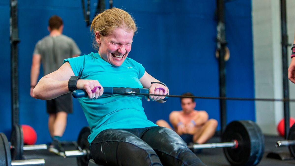 Woman in CrossFit gym rowing, face contorted with effort