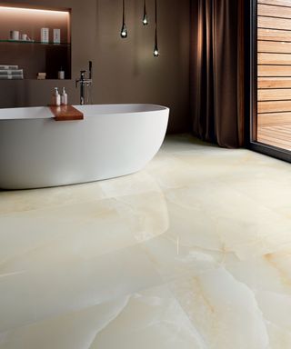 An example of small bathroom flooring ideas showing stone-loo porcelain floor tiles and a large white free-standing bath in front of a brown wall