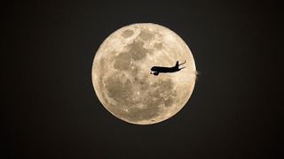 a supermoon with the silhouette of a plane flying in front