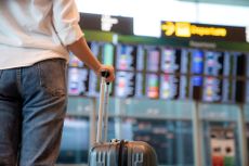 A woman with a suitcase reads an arrival and departure board at an airport