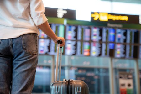 A woman with a suitcase reads an arrival and departure board at an airport