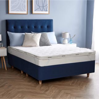 A mattress topper on a navy blue upholstered bed in a pale blue bedroom
