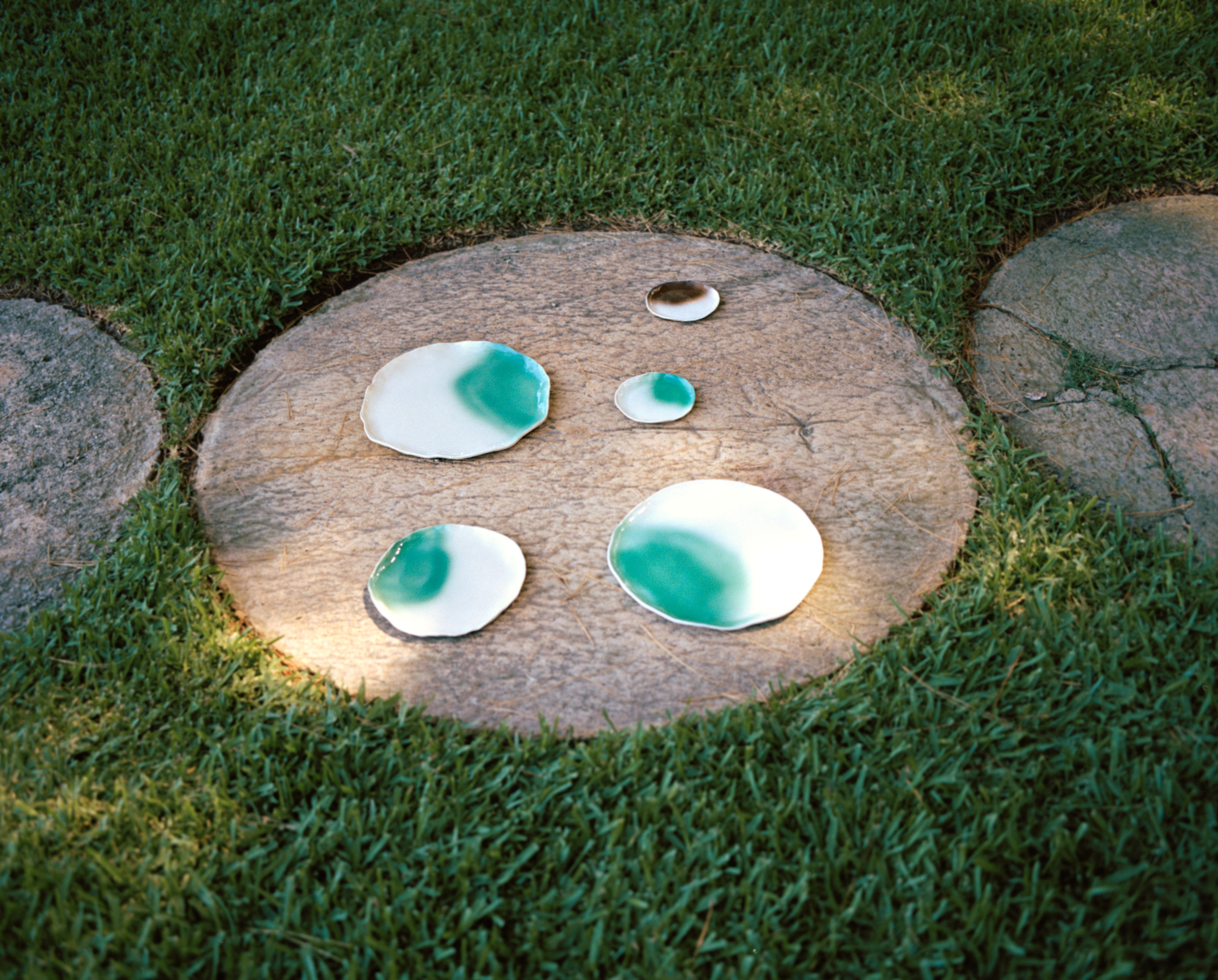 5 ceramic plates on a circular paving stone embedded in a lawn