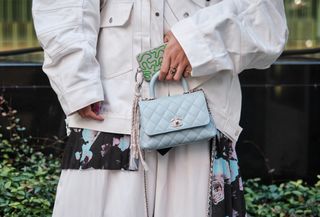 a close-up street style photo of a woman holding a crossbody cell phone bag with a white denim jacket