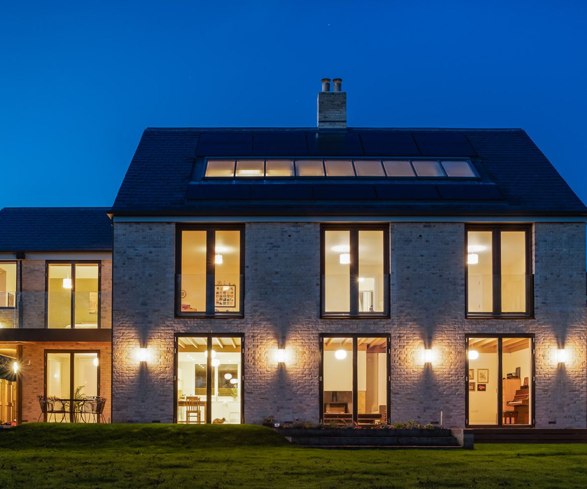 A self build home at dusk with exterior lights and interior lights on