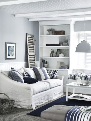 white bookcase alcove shelf, white linen couch, blue and white cushions, blue rug, pale blue walls, shiplap