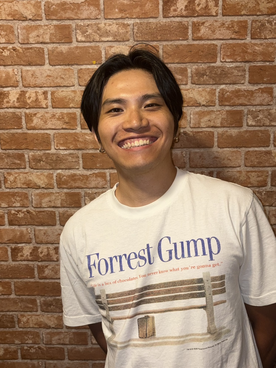 Founder of MeetMeetNow, Kazuki Nishijima, wearing a Forrest Gump T-shirt and standing in front of a brick wall