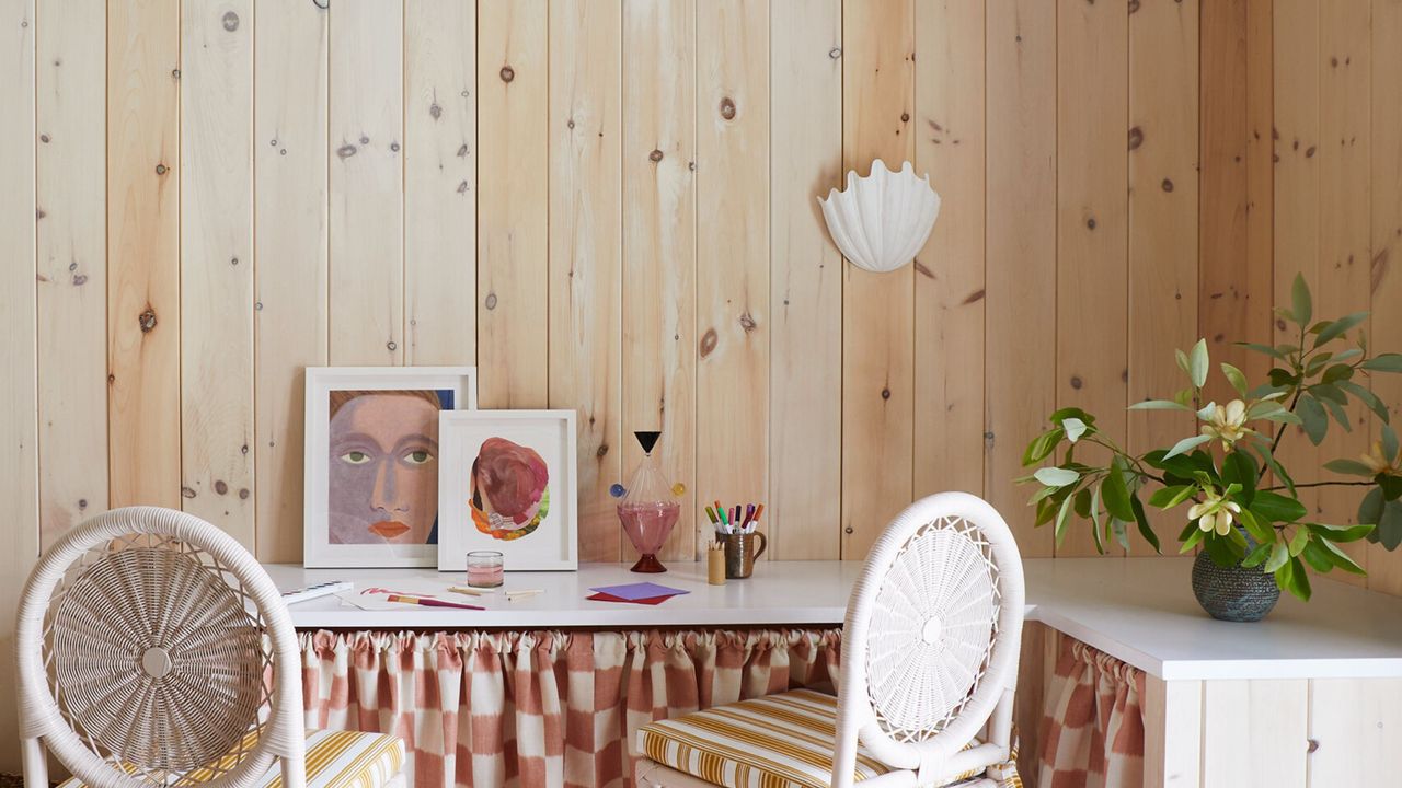 timber clad room with corner desk, two cane chairs, artwork, and checkered table skirt