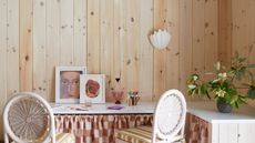 timber clad room with corner desk, two cane chairs, artwork, and checkered table skirt