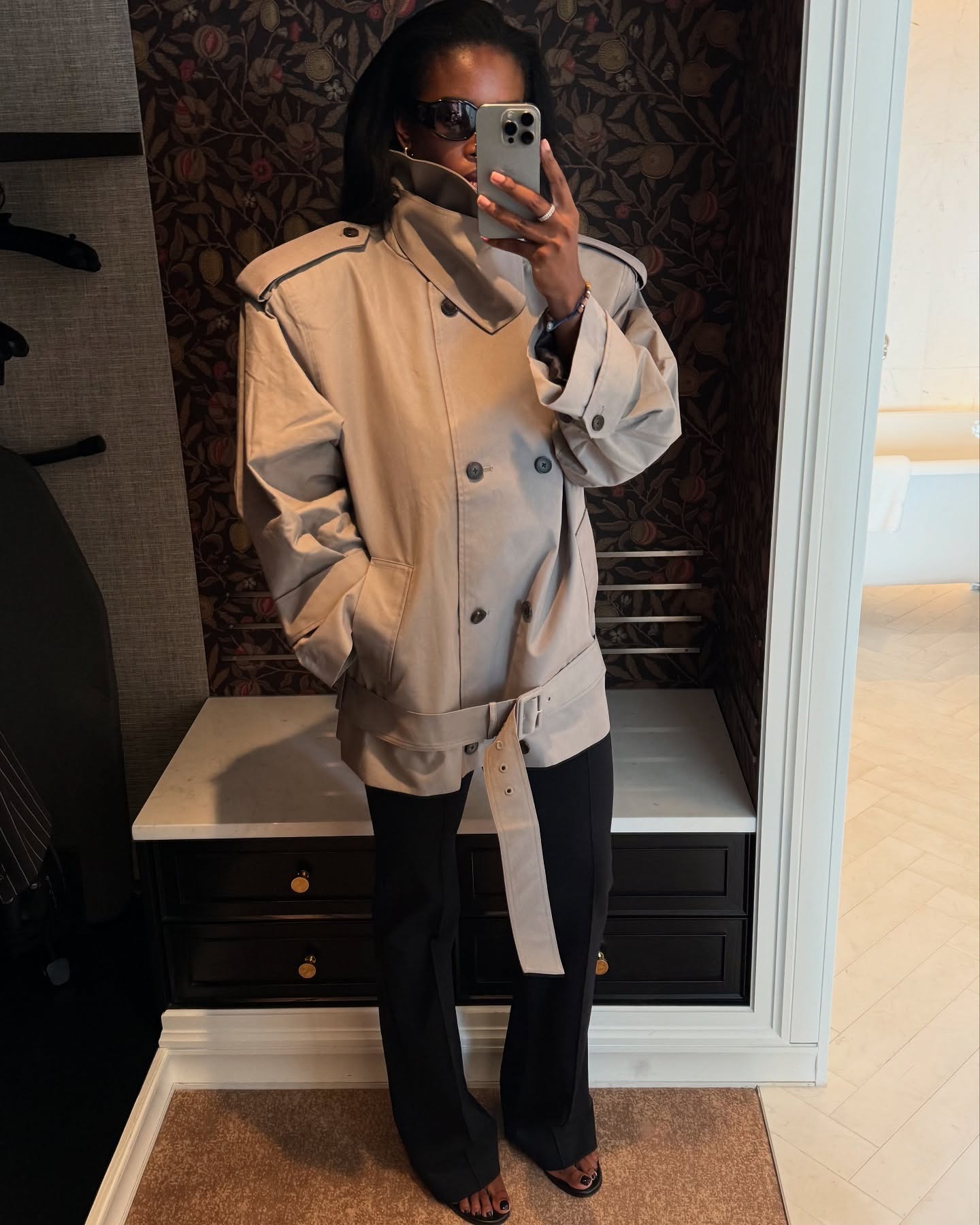 Marilyn wears a funnel-neck trench coat, black flare trousers and heels.