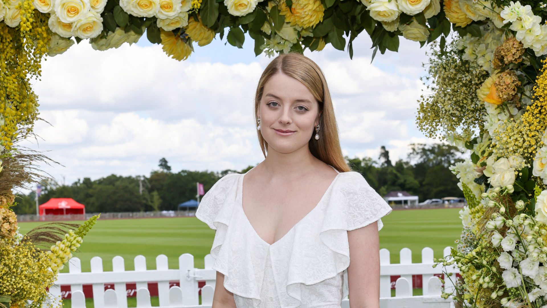 Flora Vesterberg wearing a white dress with ruffles posing in an archway of yellow flowers