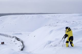 A man in a yellow ski outfit standing on a ridge with snow on it.