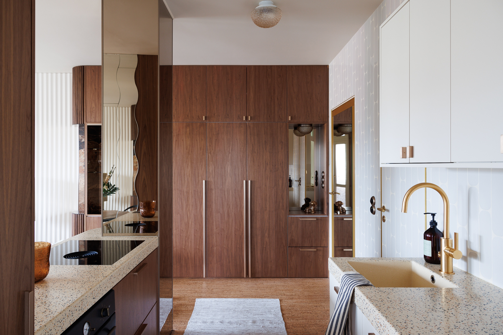 A glamorous suite fitted with reflective mirrored walls, wavy detailing, brass accents, dark woods, and plush leather and textiles.