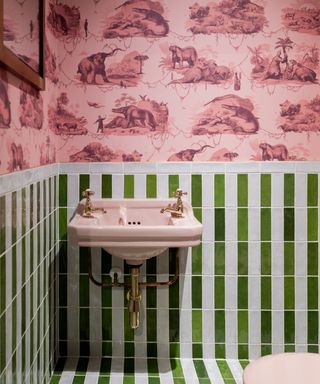 pink and green bathroom with pink wallpaper, green and white wall tiles, pink basin, gold hardware