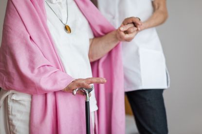 Senior woman with a crutch getting support from nurse at a nursing home.