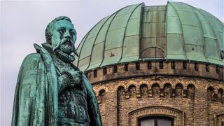 Outside a domed observatory is a bronze statue of Tycho Brahe wearing a cape.