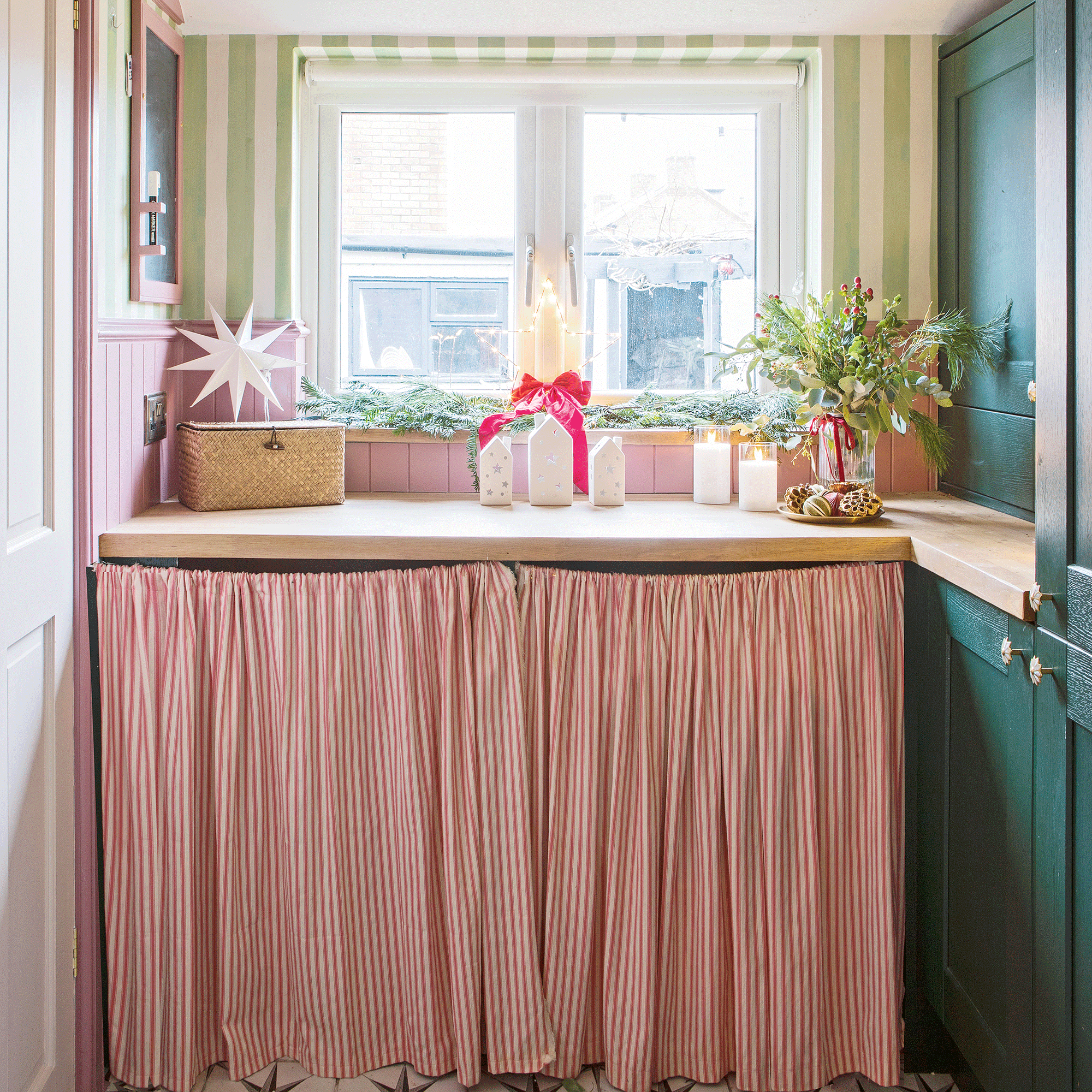 a utility area of a kitchen with a cabinet skirt in striped fabric , green cabinet doors and a window
