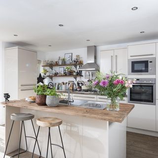 white island with wooden worktop and stools, white cabinets, wooden shelving, steel extractor fan