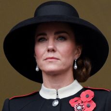 Kate Middleton wearing a black hat, black coat with a white collar and red poppy brooches looking serious