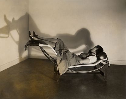 An image of Charlotte Perriand on the ‘Chaise longue basculante B306’. Woman lying on the chaise lounge, with her legs lifted, looking at the wall.