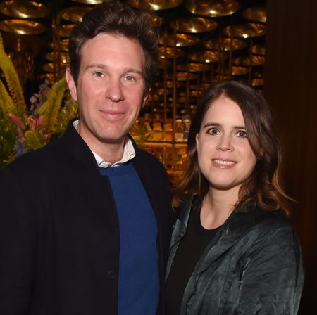 Princess Eugenie and Jack Brooksbank smiling at the camera in front of a floral display