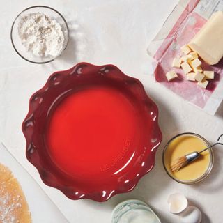 Red Le Creuset pie dish on table, cooking accessories surrounding