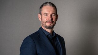 NCC Group CEO Guy Ellis pictured wearing a dark navy suit and shirt.
