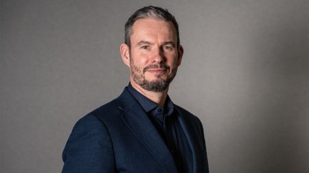 NCC Group CEO Guy Ellis pictured wearing a dark navy suit and shirt.