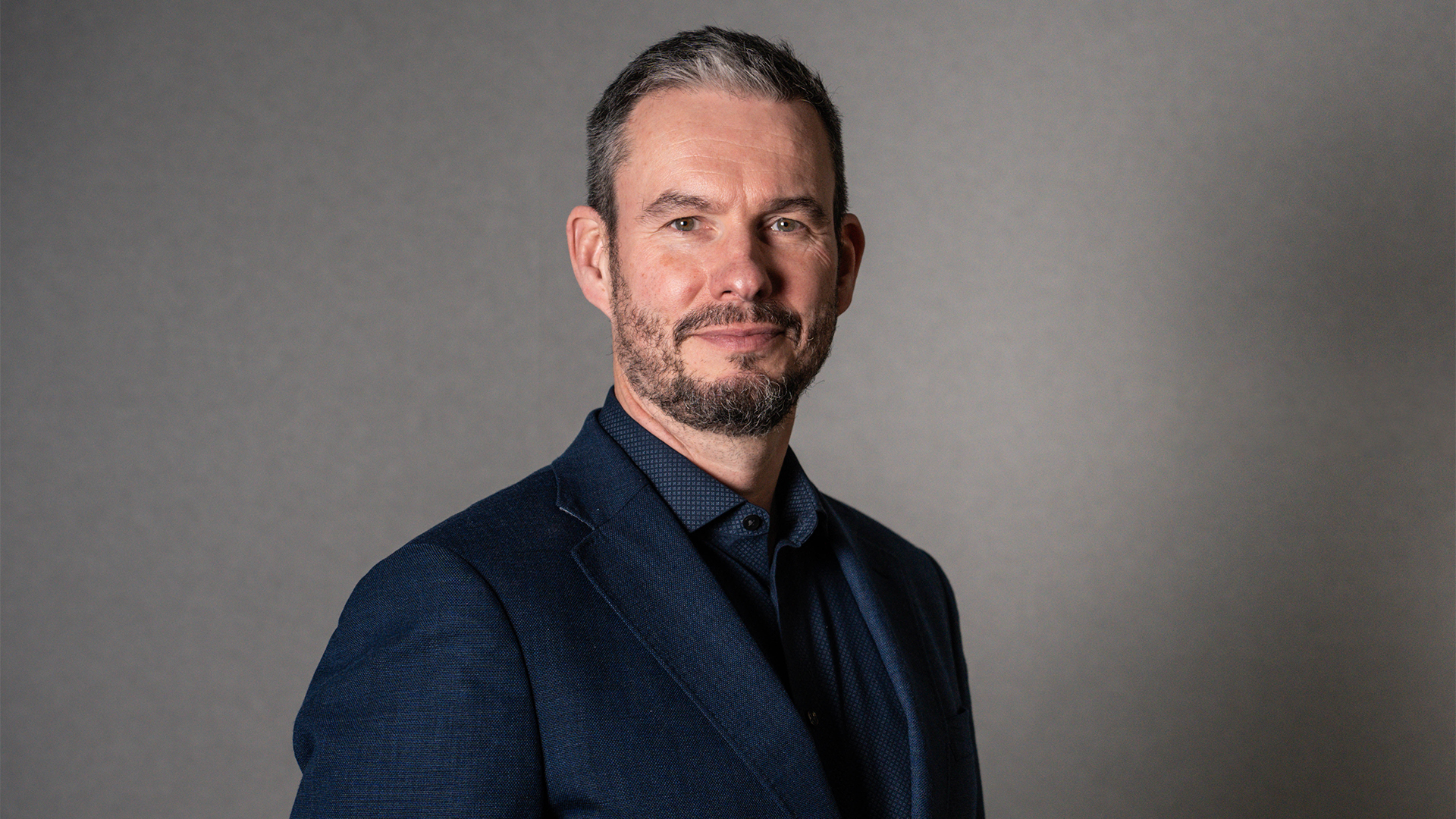 NCC Group CEO Guy Ellis pictured wearing a dark navy suit and shirt.