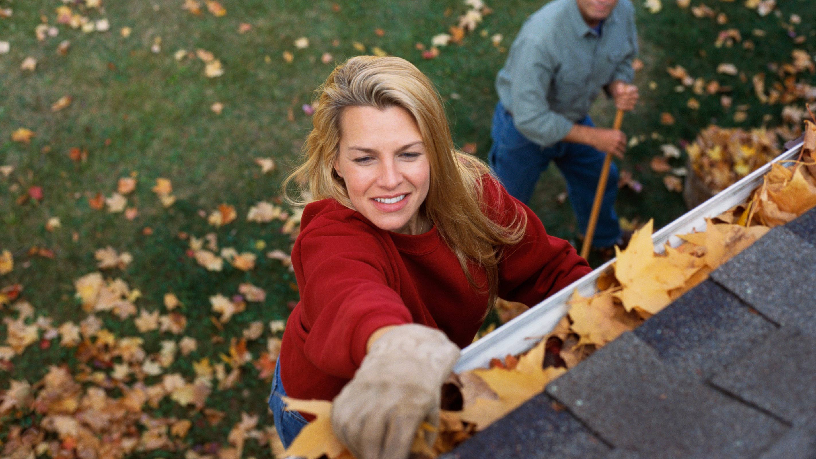 Frau räumt Blätter aus Dachrinnen