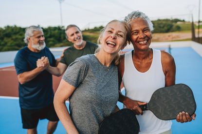 Four older people smile after a pickleball game. There are two women in the front of the camera and two men behind.