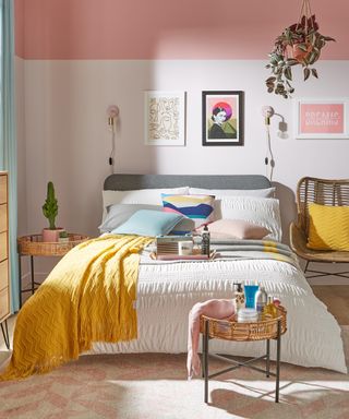 A modern bedroom with framed wall decor, hanging indoor houseplant, mustard yellow throw and pink wall paint decor