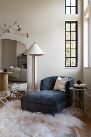 Corner of a room with dark blue velvet chaise, cream floor lamp and sheepskin rug