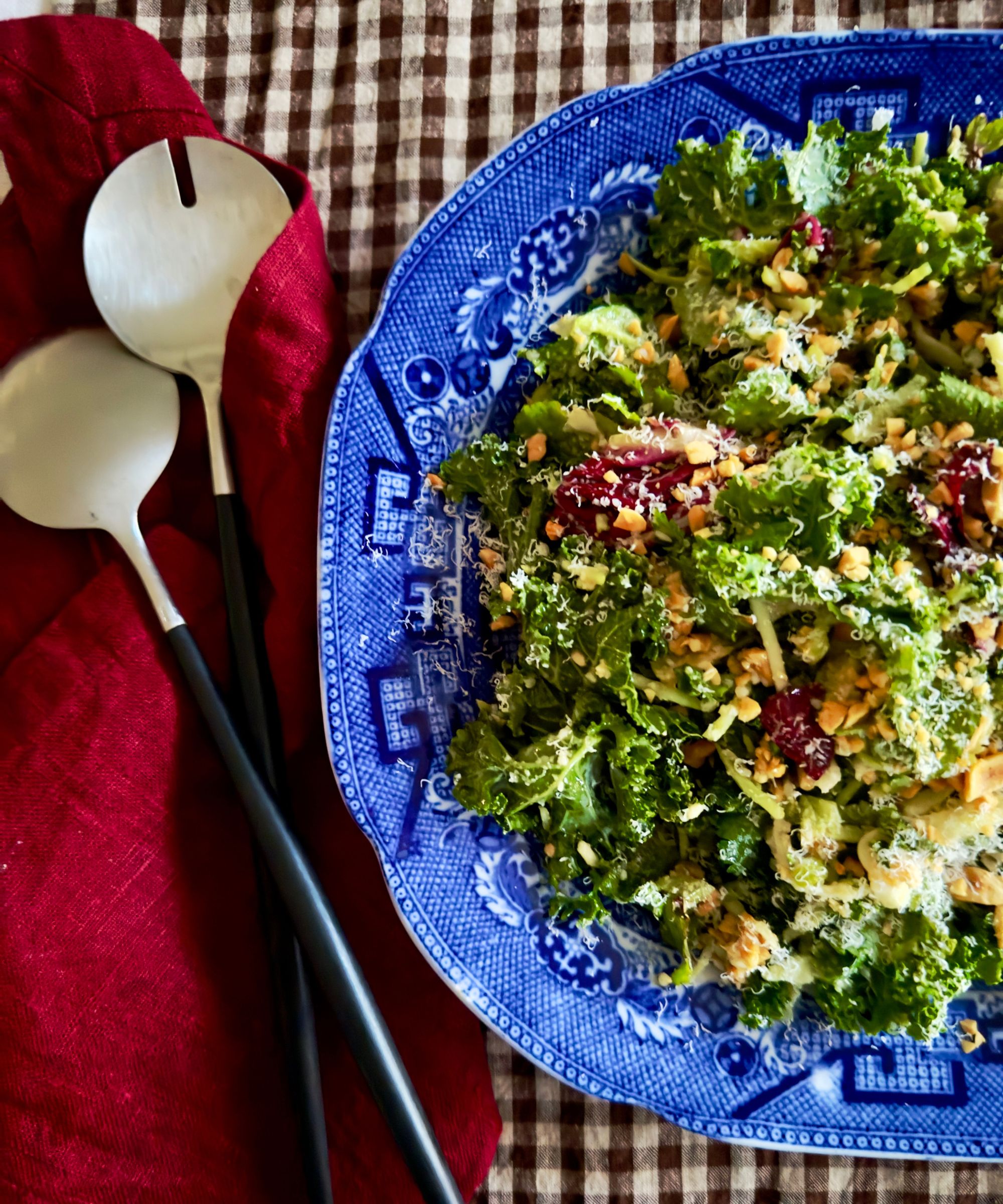 Crunchy green salad in a blue vintage dish on a gingham tablecloth with a red napkin and salad servers