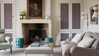 living room with cream patterned carpet, comfy sofas, built in storage in alcove and large cream fireplace with black grate