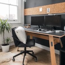 home office with black and white walls, wood floor, corkboard strip, black office chair at wood table with black top, computer, bare hanging lights, and potted plant