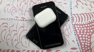 A pair of AirPods sit on top of two stacked Samsung phones
