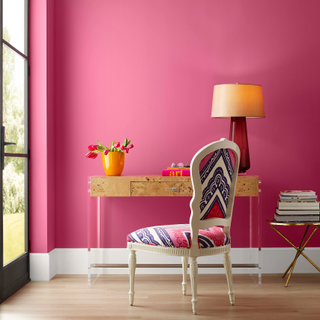 A study space with bright pink walls and a burl wood desk