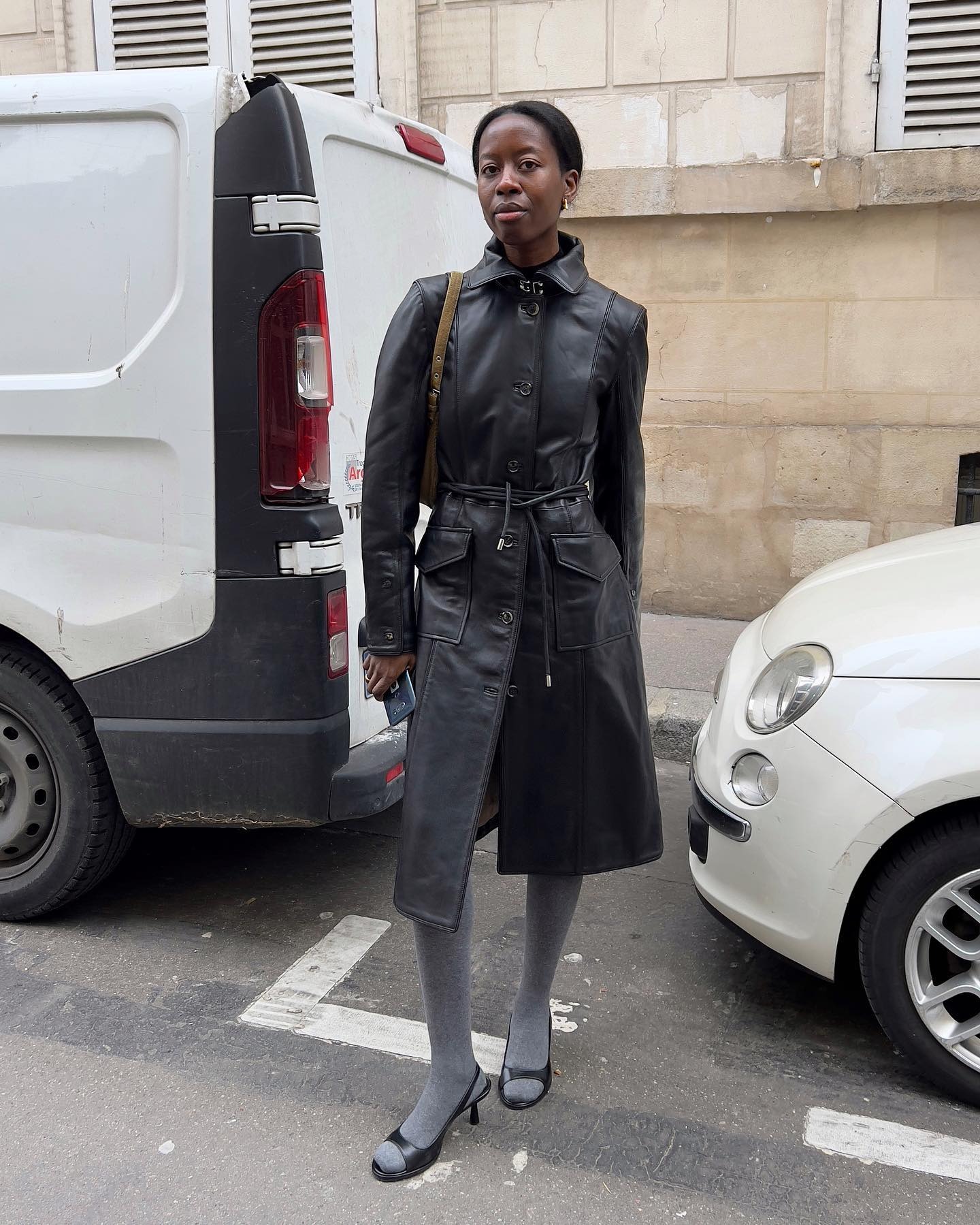 Influencer @sylviemus_ wears grey tights with peep-toe shoes and a black leather trench coat.